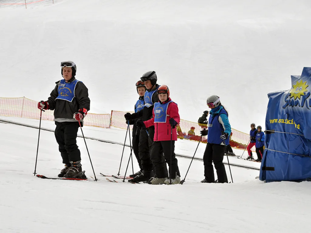 Gruppe steht auf Skiern vor einer Hüttenwand.